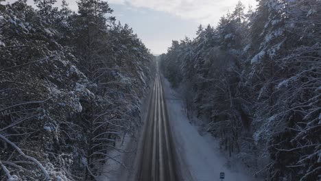 Aerial-view-of-a-snowy-forest-road-in-Lithuania-during-winter-with-distant-cars-approaching