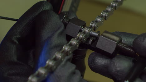Bicycle-mechanic-uses-tool-to-insert-link-into-bike-chain,-close-up