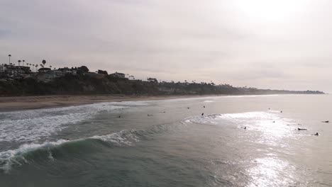 Aerial-Morning-View-of-Calfornia-surfers-riding-waves-in-OC-beach-town