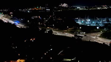Ambulance-with-constant-blue-lights-zooms-racing-past-cars-on-highway-above-bridge-in-tropical-city-at-night,-drone-of-Curacao