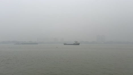 Few-merchant-ships-and-boats-stationed-on-Hooghly-river-with-foggy-view-during-morning-of-Kolkata,-India