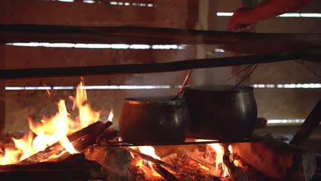A-cooking-pot-is-placed-above-a-raw-flame-while-someone-stirs-the-food-inside