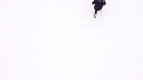 Aerial-view-of-man-walking-in-snow-while-holding-a-remote-controller