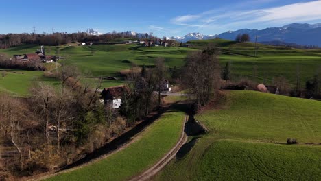 Lush-green-fields-in-jona-with-glarus-alps-in-the-background,-clear-sky,-aerial-view