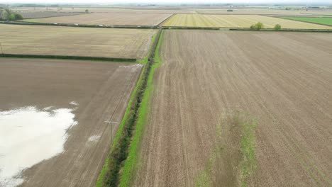Drone-footage-flying-over-ploughed-fields,-along-hedgerows-and-over-a-minor-road