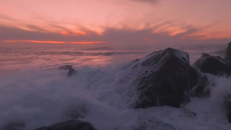 Lebendige-Farben-Des-Sonnenuntergangs-Mit-Einigen-Heftigen-Wellen,-Die-Gegen-Felsen-Schlagen