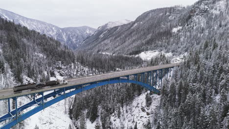 Winter-Ballet:-Cars-Glide-Across-Paulson-Bridge,-Snow-Blanketed-Peaks-Rise