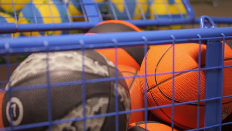 Assorted-sports-balls-behind-blue-mesh-cage-in-a-storage-room,-blurred-background