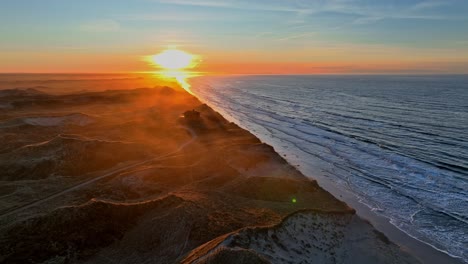 Panoramiv-view-The-beach-is-washed-by-sea-waves,-high-dunes-have-formed,-the-summer-house-standing-on-the-dunes-is-surrounded-by-a-mystical-mist,-and-the-sun-is-setting-on-a-winter-evening