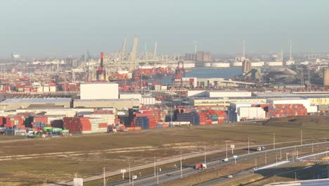 Zoomed-aerial-lifting-view-of-trucks-driving-over-the-highway-with-in-the-backdrop-the-port-of-Rotterdam