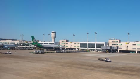 Outside-exterior-view-of-international-building-terminal,-tarmac-runway,-parked-airplanes,-cargo-baggage-trucks-and-transport-at-Taiwan-Taoyuan-International-Airport