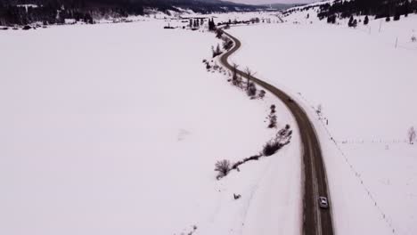 Die-Kamera-Neigt-Sich-Nach-Oben-Und-Zeigt-Zwei-Autos,-Die-Sich-Auf-Einer-Kurvenreichen-Straße-In-Einer-Schneebedeckten-Landschaft-Bewegen