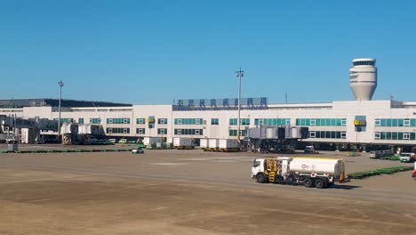 Exterior-view-of-Taiwan-Taoyuan-International-Airport-terminal-building-and-airplane-fuel-tanker-truck-on-driving-along-tarmac-runway