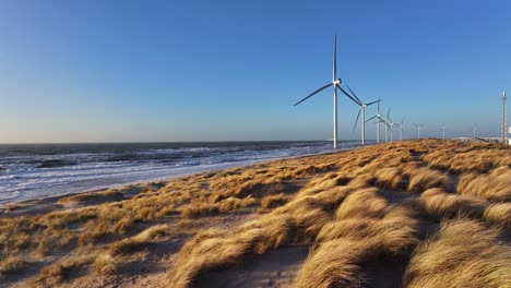 Slowmotion-dolley-view-over-orange-colored-dunes-while-windmills-rotate-in-the-wind