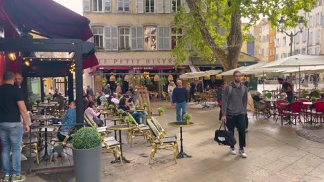 Bustling-outdoor-cafe-scene-in-Aix-en-Provence-with-patrons-dining,-chatting,-European-architecture-backdrop,-daylight