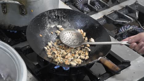 Chef-stir-frying-mussels-in-a-wok-over-a-high-flame-in-a-commercial-kitchen,-action-shot