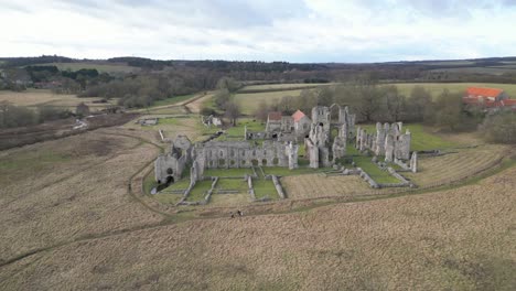 Castle-acre-priory-ruins-in-norfolk,-with-surrounding-fields-and-a-clear-sky,-aerial-view