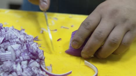 Close-up-of-hands-chopping-red-onion-on-a-yellow-cutting-board,-kitchen-setting