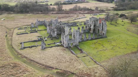 Castle-acre-priory-ruins-amidst-green-fields-on-a-cloudy-day,-aerial-view