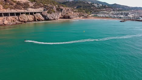 Skate-surfer-creating-ripples-on-the-turquoise-waters-near-port-ginesta,-barcelona,-aerial-view