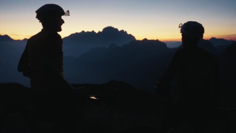 two-male-bicycle-riders-fist-bump-in-the-dark-sunset-in-the-mountains-on-the-top-of-the-hill