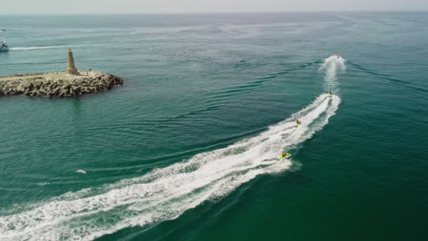 Jet-skis-racing-near-a-lighthouse-at-puerto-banus,-marbella,-aerial-view