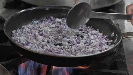 Chopped-red-onions-sautéing-in-a-pan-over-a-gas-flame,-cooking-process-in-action,-kitchen-setting