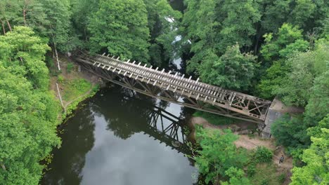 Observe-the-striking-sight-of-a-broken-bridge-nestled-within-the-forest,-captured-from-an-aerial-perspective,-offering-a-unique-view-of-nature's-resilience-in-this-captivating-stock-footage