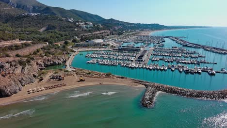 Port-Ginesta-Marina-Voller-Boote-Mit-Strand-Und-Wellenbrecher,-In-Der-Nähe-Von-Barcelona,-Spanien,-Sonniger-Tag,-Luftaufnahme