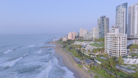 Umhlanga-coastline-with-modern-buildings-and-a-lighthouse,-early-morning-light,-aerial-view