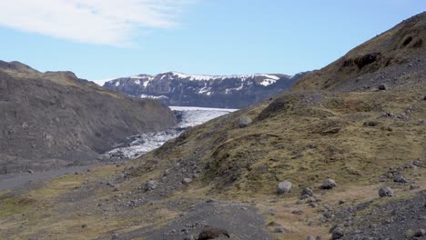 Paisaje-Islandés-Con-Glaciar-Entre-Montañas,-Colinas-Verdes-Cubiertas-De-Musgo-Bajo-Un-Cielo-Azul