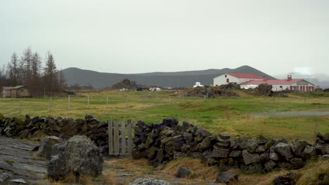 Rural-Icelandic-farm-with-lava-rock-fence,-overcast-sky,-and-distant-mountains,-static-shot