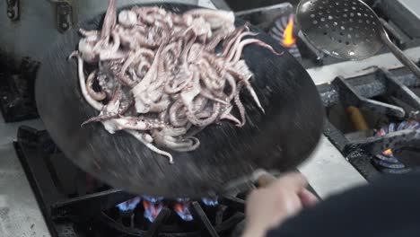 Chef-tossing-octopus-in-a-wok-over-high-flame,-kitchen-action