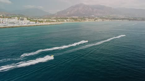 Jet-skis-racing-near-puerto-banus-in-marbella-with-scenic-mountains,-aerial-view