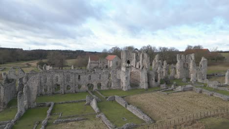 Castle-acre-priory-ruins-in-norfolk,-clouds-adorn-the-sky,-aerial-view