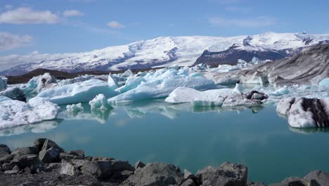 Icy-glacial-lagoon-with-floating-icebergs-under-blue-sky-in-Iceland,-clear-reflection-on-water