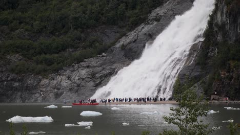 Tourists-taking-pictures-with-Nugget-Falls,-Mendenhall-Glacier,-Alaska