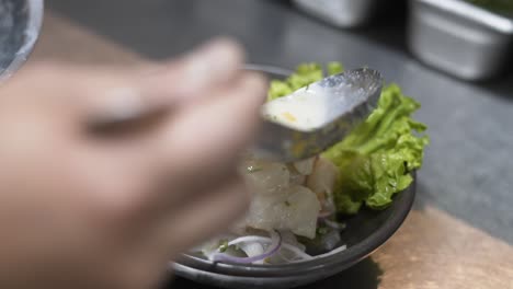 Close-up-shot-of-a-hand-preparing-fresh-ceviche-with-lime,-onion,-and-lettuce