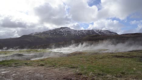 Geothermische-Aktivität-In-Island-Mit-Dampf,-Der-Vor-Dem-Hintergrund-Von-Bergen-Und-Einem-Bewölkten-Himmel-Aus-Dem-Boden-Aufsteigt