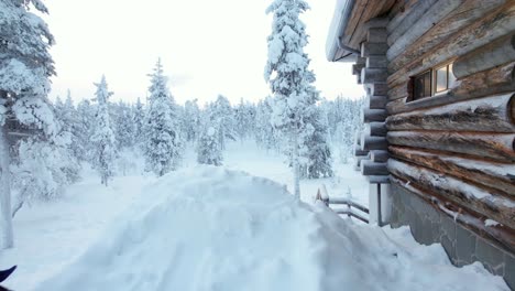 Girl-Looks-Out-Into-Snowy-Landscape,-Standing-Beside-Cabin-in-Lapland,-Finland,-Arctic-Circle