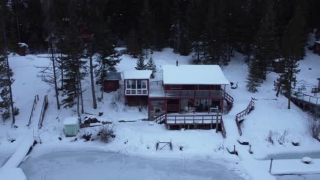 Esta-Hermosa-Casa-De-Madera-Cubierta-De-Nieve-Se-Encuentra-Junto-A-Un-Lago-Congelado-Y-Un-Denso-Bosque-En-Columbia-Británica