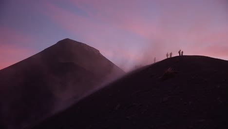 People-on-ridge-of-Fuego-volcano-get-hit-by-dust-and-strong-winds-during-breathtaking-sunset-with-pink-clouds,-Guatemala