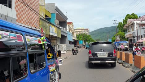 Driving-on-town-street-full-of-people,-traffic,-shops-and-colorful-bus-on-Alor-Island-in-Lesser-Sunda-Islands-of-East-Nusa-Tenggara
