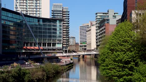 Cable-stayed-pedestrian-bridge-in-Manchester-crosses-river-below-urban-buildings