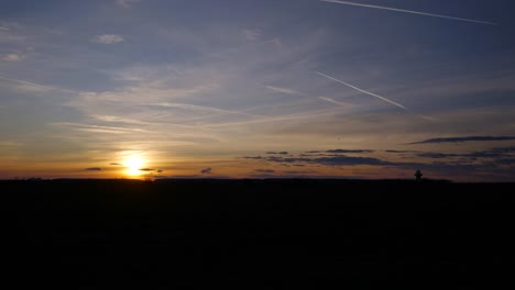 Spektakulärer-Sonnenuntergang-über-Der-Grünen-Wiese-Mit-Wolken-Und-Flugzeugspur