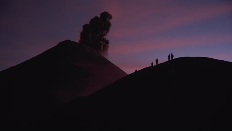 Silhouetted-group-of-people-witnesses-massive-lava-eruption-on-ridge-of-Fuego-volcano-during-vibrant-twilight