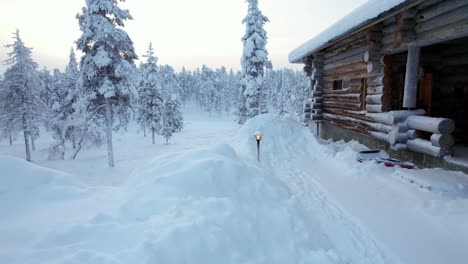 Girl-Is-Revealed-Walking-In-Snowy-Winter-Wonderland-Landscape,-With-Cabin,-and-Landscape-Lights-In-Lapland,-Finland,-Arctic-Circle
