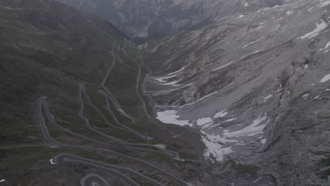 Drone-shot-flying-over-the-Stelvio-Pass-Italy-on-a-grey-day-going-to-the-scenic-view-of-the-snowy-mountains-in-the-background-on-a-grey-day-during-sunset-time-LOG