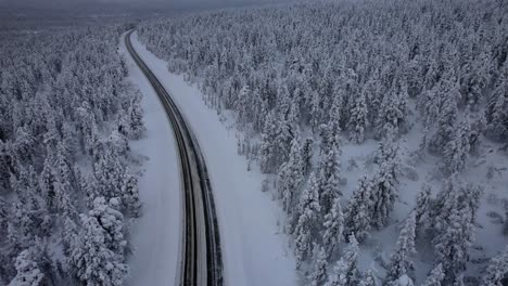 Aerial-Drone-View-Of-Road-Surrounded-by-Winter-Wonderland-Forest-in-Lapland,-Finland,-Arctic-Circle