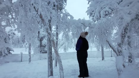 Girl-Looking-Up-Under-Trees-In-Snowy-Forest-In-Lapland,-Finland,-Arctic-Circle